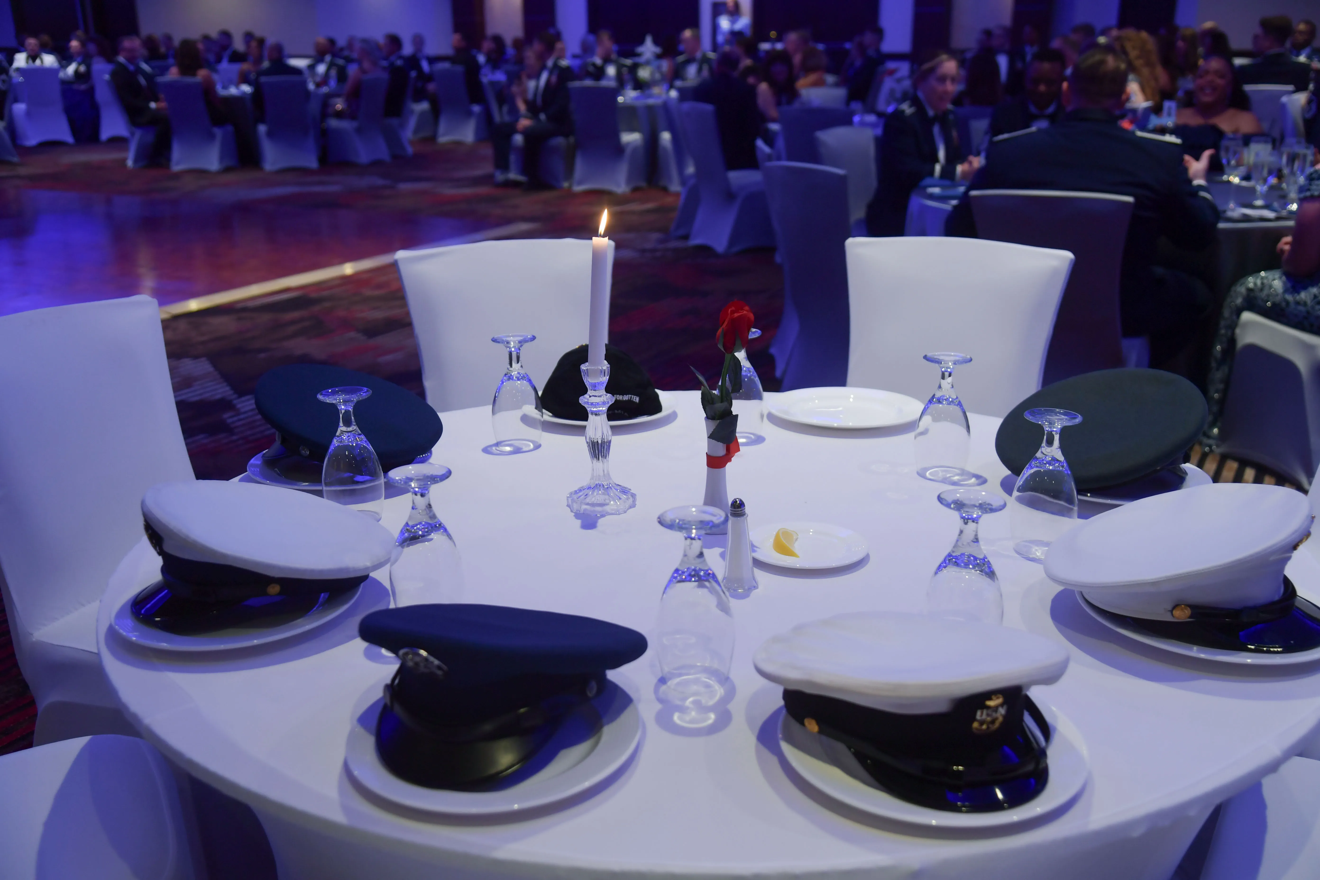 A POW/MIA remembrance table set with military service caps, a candle, and a red rose at a formal banquet