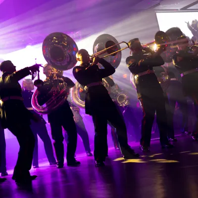 Military band members playing tubas, silhouetted in purple stage light